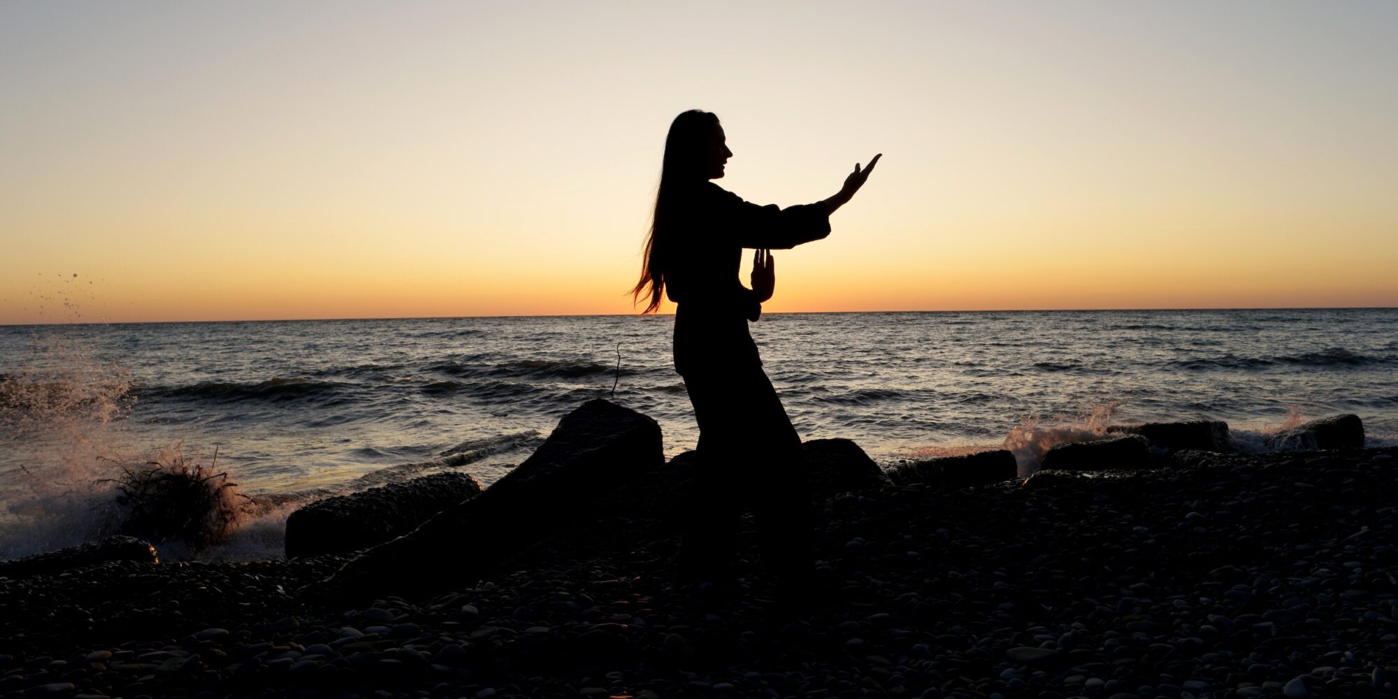 Young woman performing Wing Chun stance on the beach at sunset time. Concept of sports lifestyle
