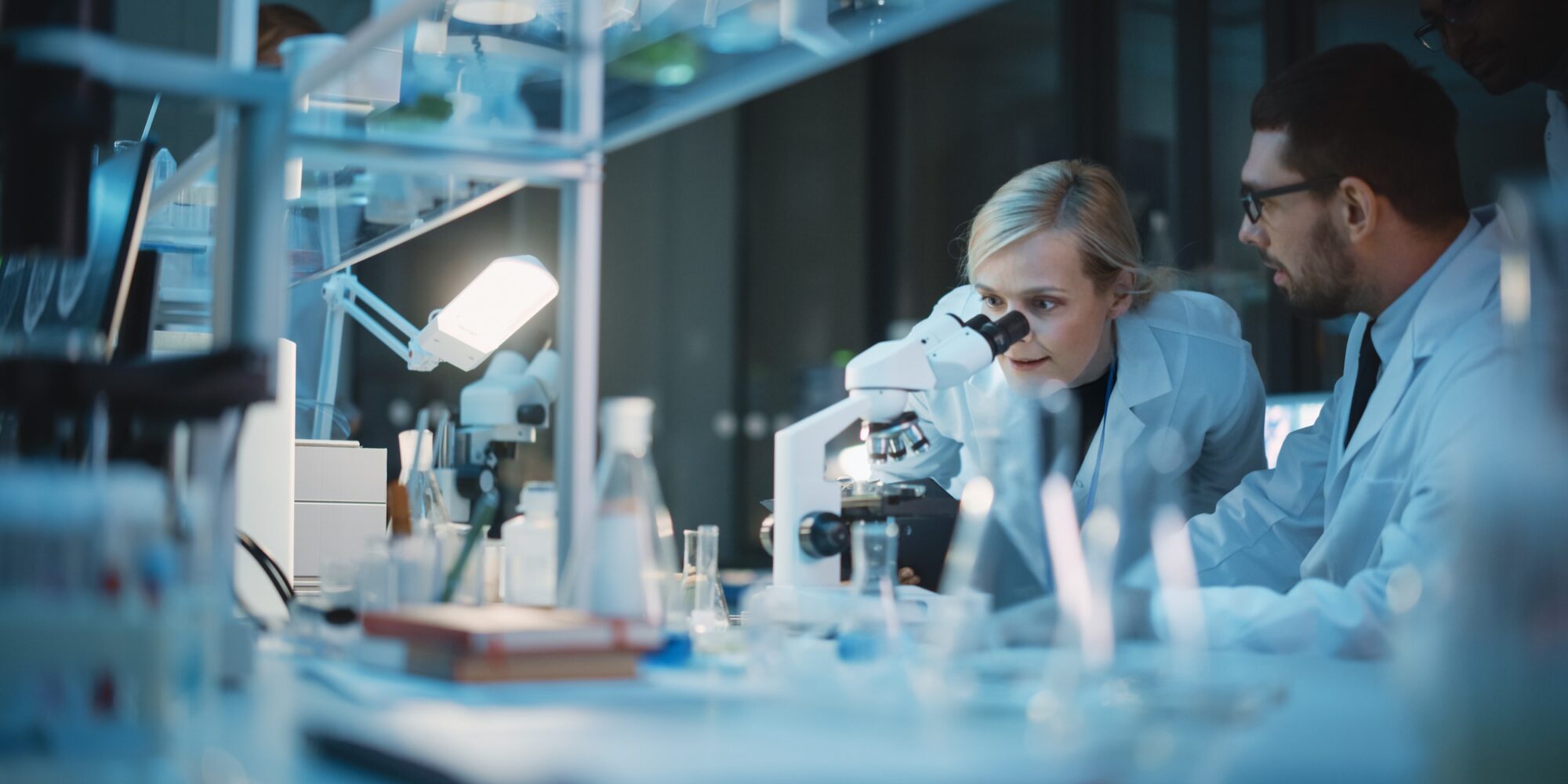 Medical Development Laboratory: Team of Female and Male Scientist Using Microscope, Analyzes Petri Dish Sample. Specialists Working on Medicine, Biotechnology Research in Advanced Pharma Lab