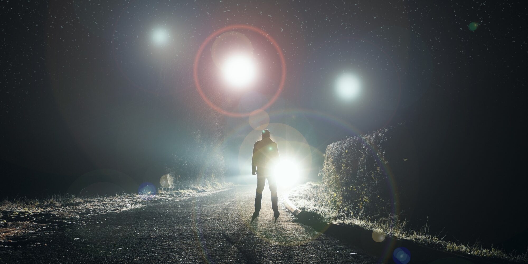UFO concept. Glowing orbs, floating above a misty road at night. With a silhouetted figure looking at the lights.