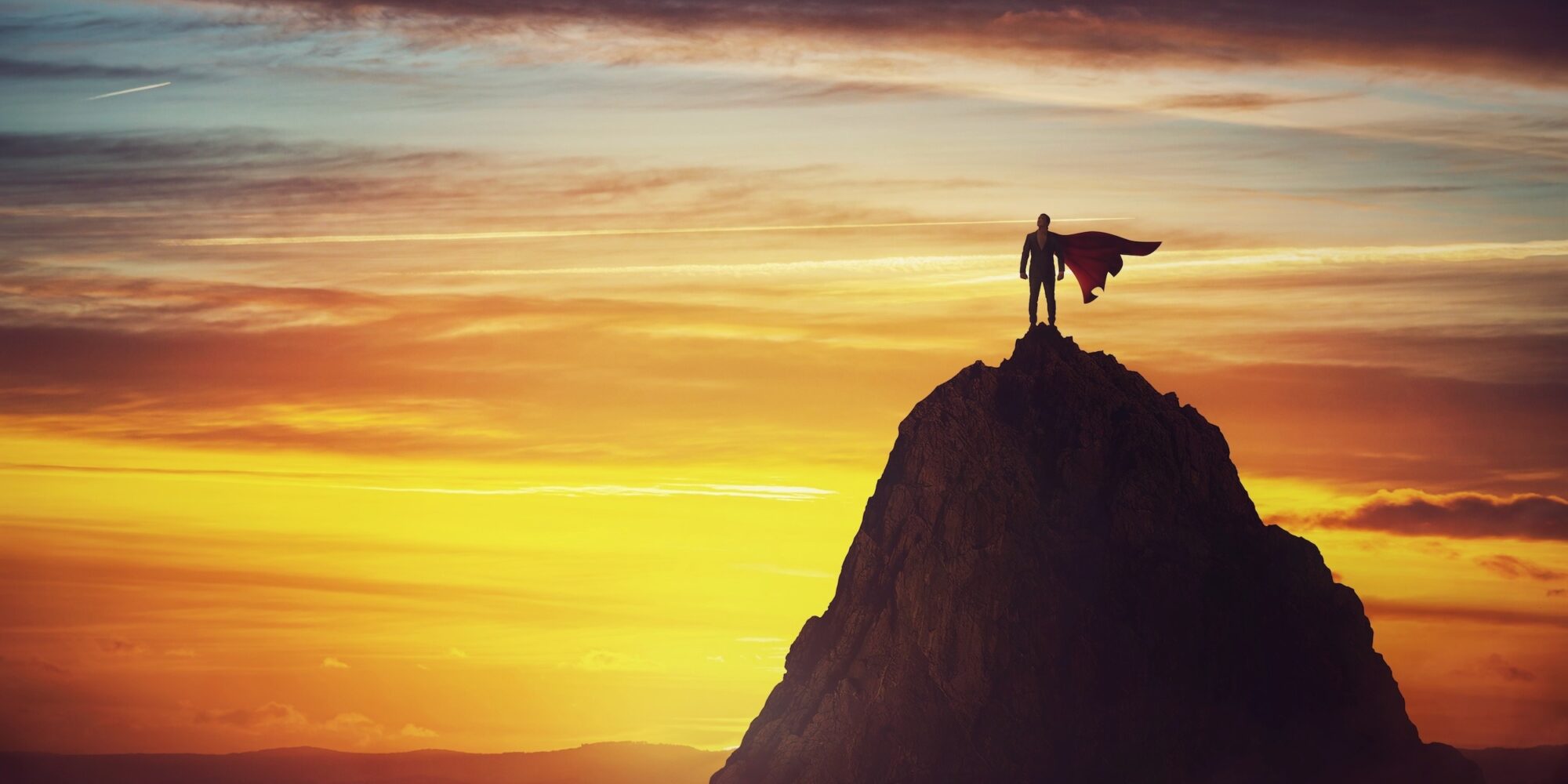 Businessman superhero conceptual scene. Determined hero with red cape stands brave on a mountain peak. Business leadership, ambition and strength metaphor. Overcome obstacles and achieve success